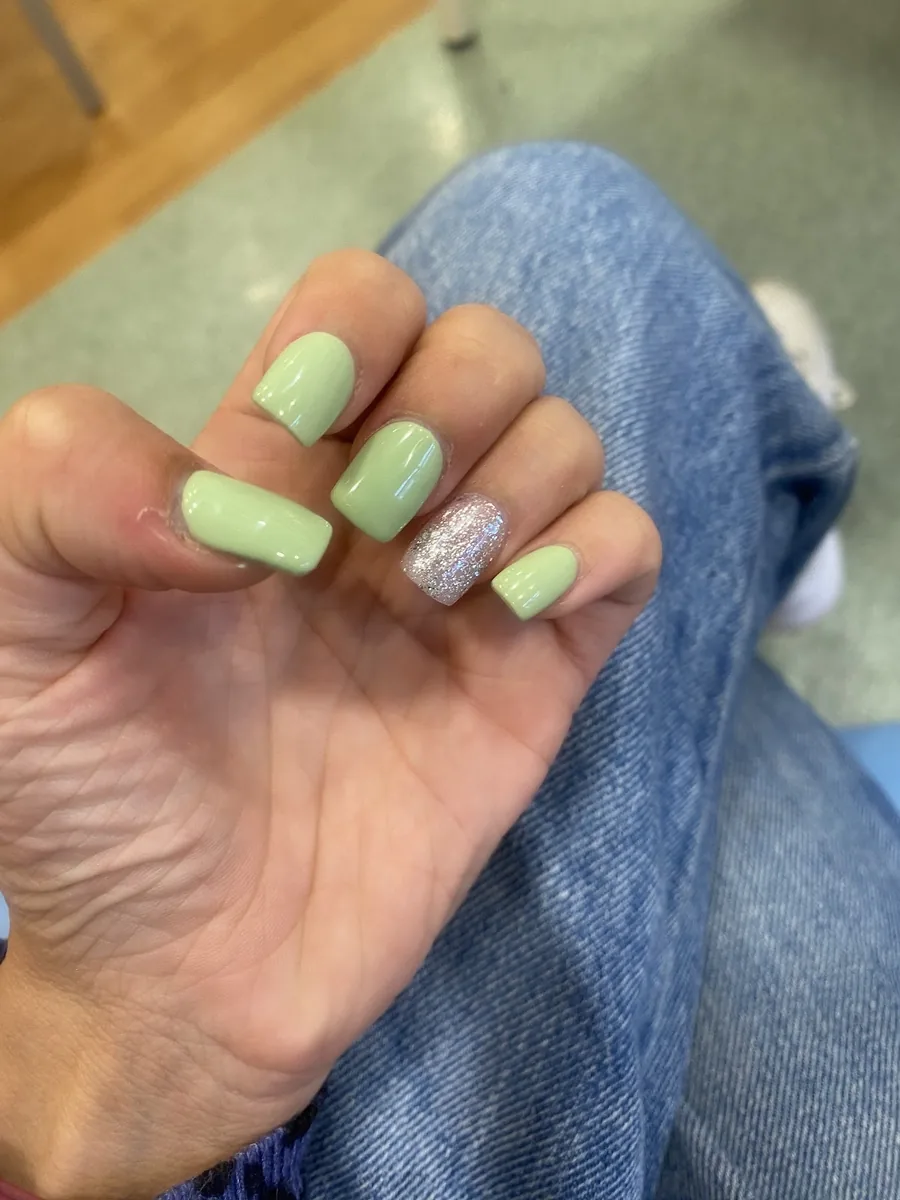 A pastel green square manicure with one glitter accent nail, hand resting on denim