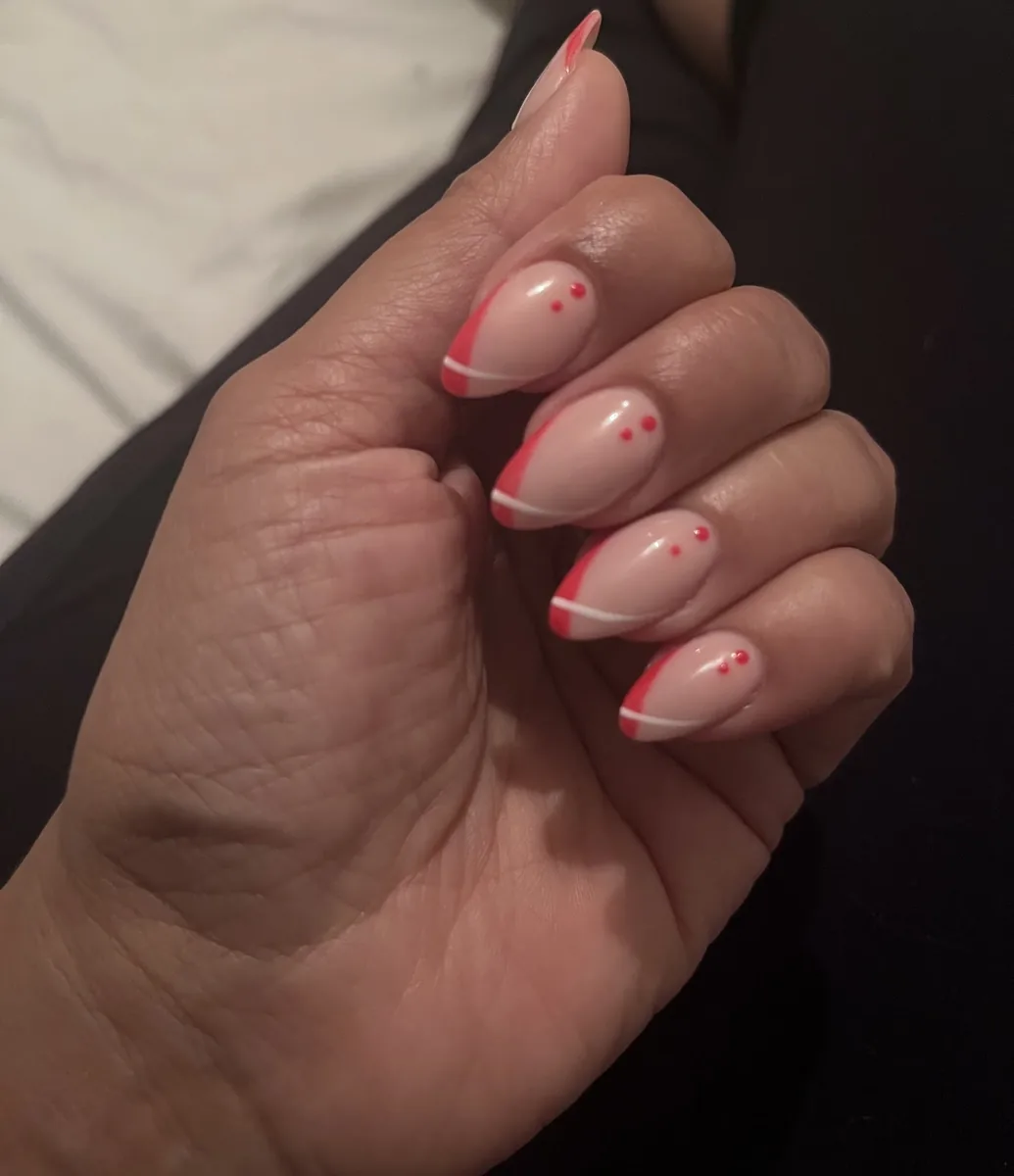 A nude gel base with coral-red French tips and small hand-painted dots